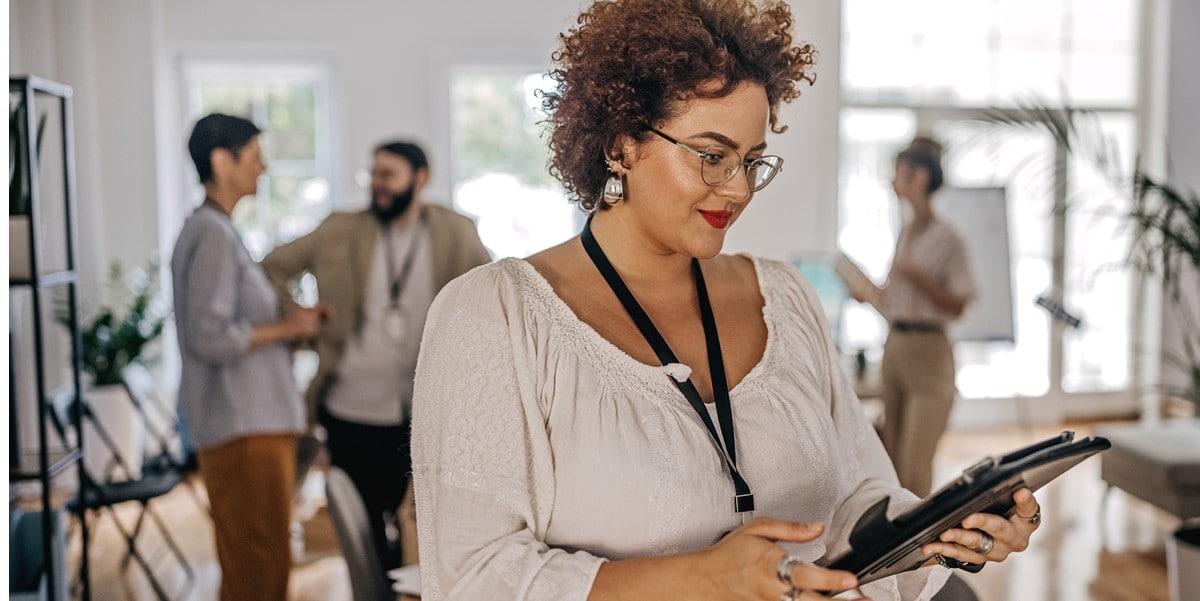 woman in office looking at tablet, colleagues in the background