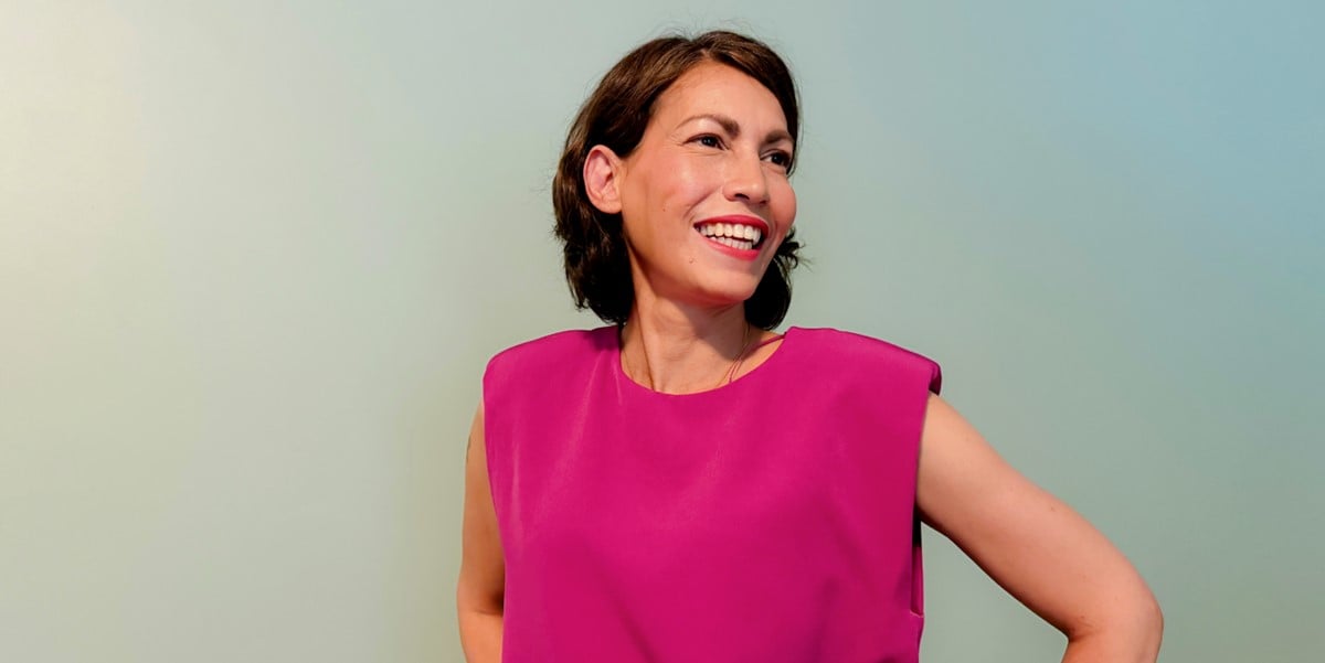 woman in hot pink top smiling, in front of blue background