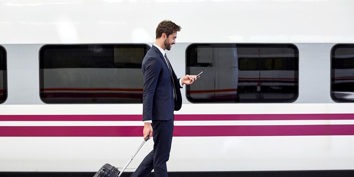 traveler with luggage, looking at phone, standing next to train